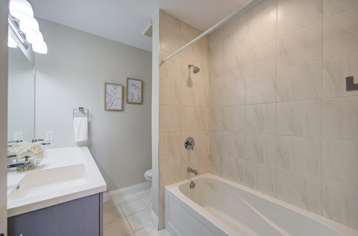 A cleaned bathroom with a white tub, beige tile surround and a clear vanity counter