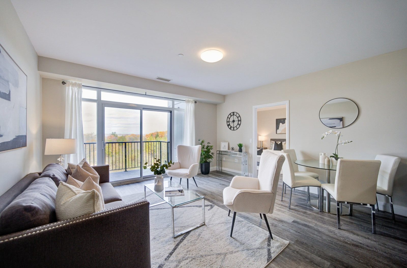 A bright condo living and dining room after a Klein's clean, with a glass coffee table, white chairs and a balcony door looking out over trees