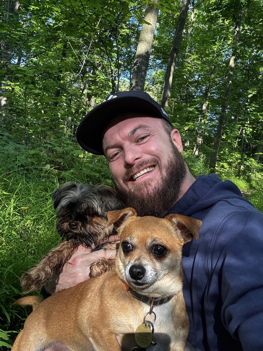 Klein's founder smiling outdoors in a green wood, holding two small dogs