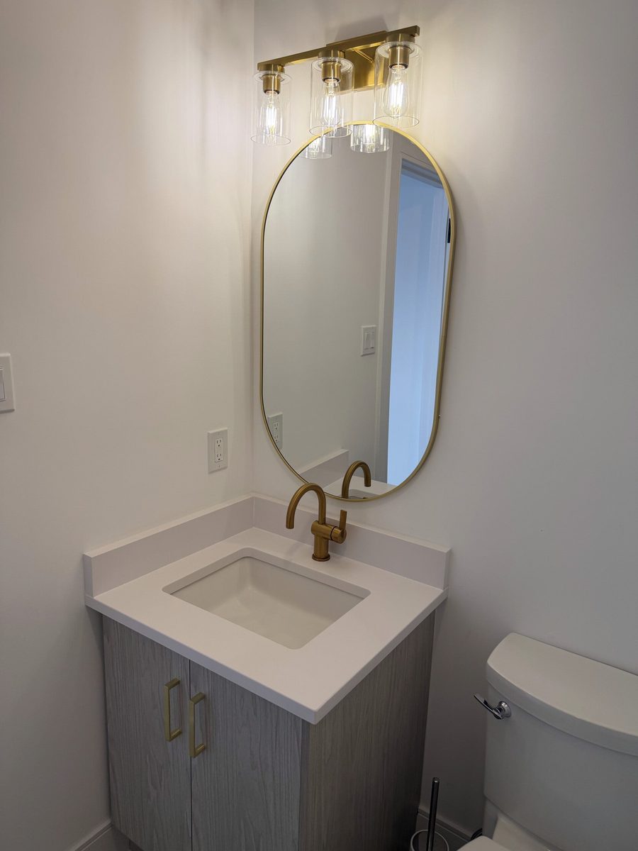 A powder room after a deep clean, with an oval gold-framed mirror, brass tap and a white quartz vanity top